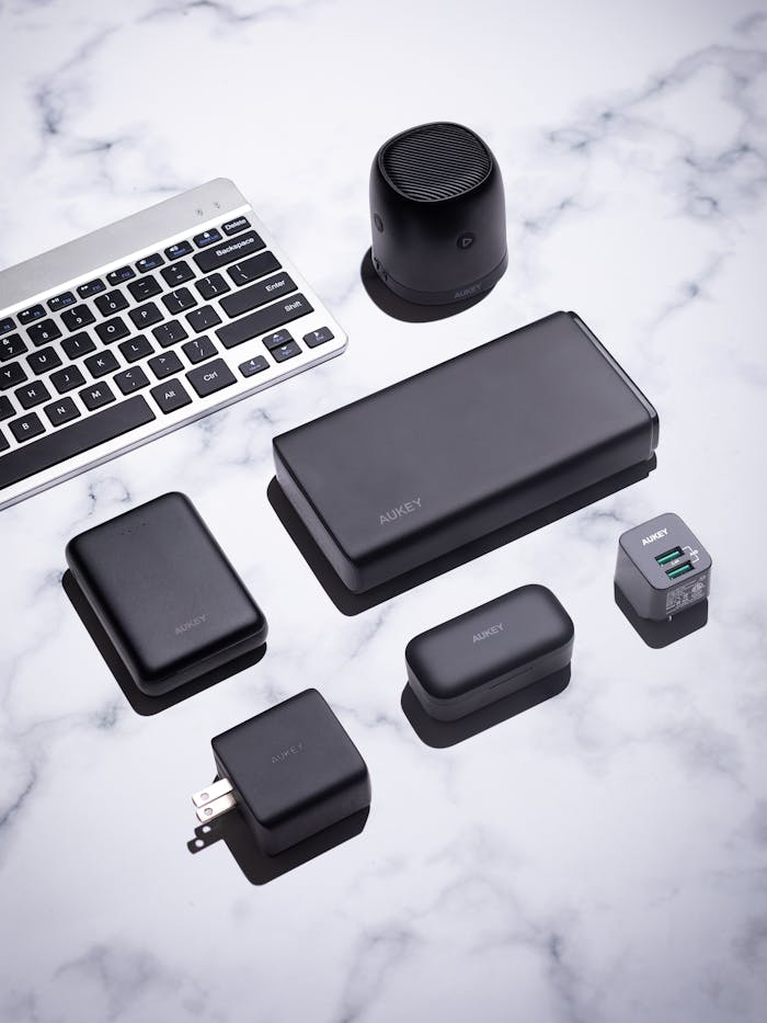 A collection of sleek black tech gadgets on a marble surface, featuring a keyboard and wireless speaker.