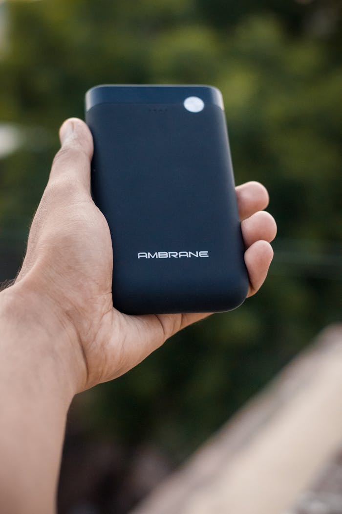 Close-up of a hand grasping a sleek black power bank with AMBRANE branding, set against an outdoor background.